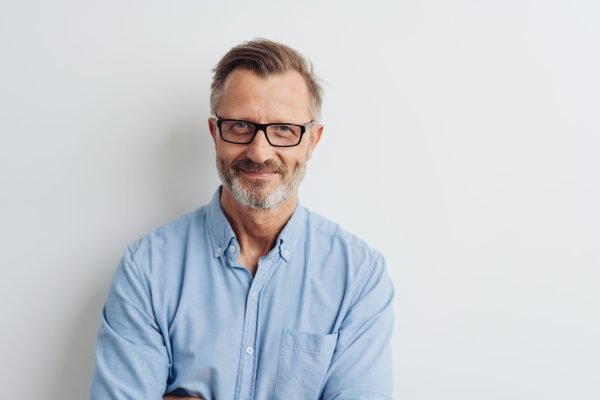 Bearded middle-aged man wearing glasses posing over a white studio background with copy space looking at the camera with a friendly smile