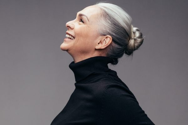 Side view of senior woman laughing on gray background. Profile view of mature woman in black casuals looking happy